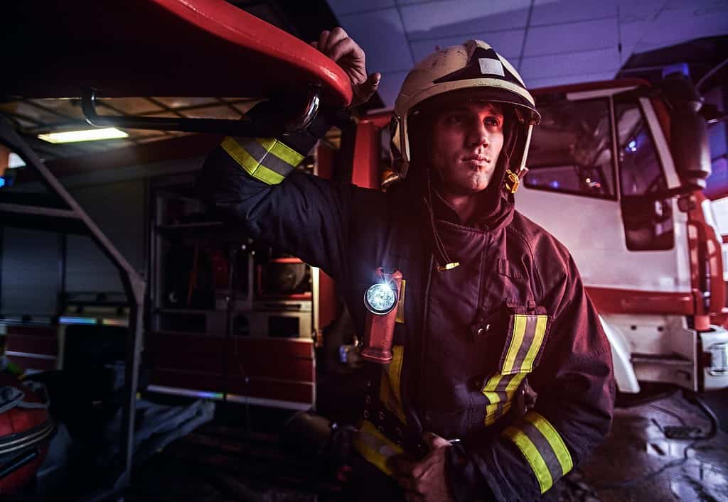 Fireman wearing protective uniform standing next to a fire engine in a garage of a fire department