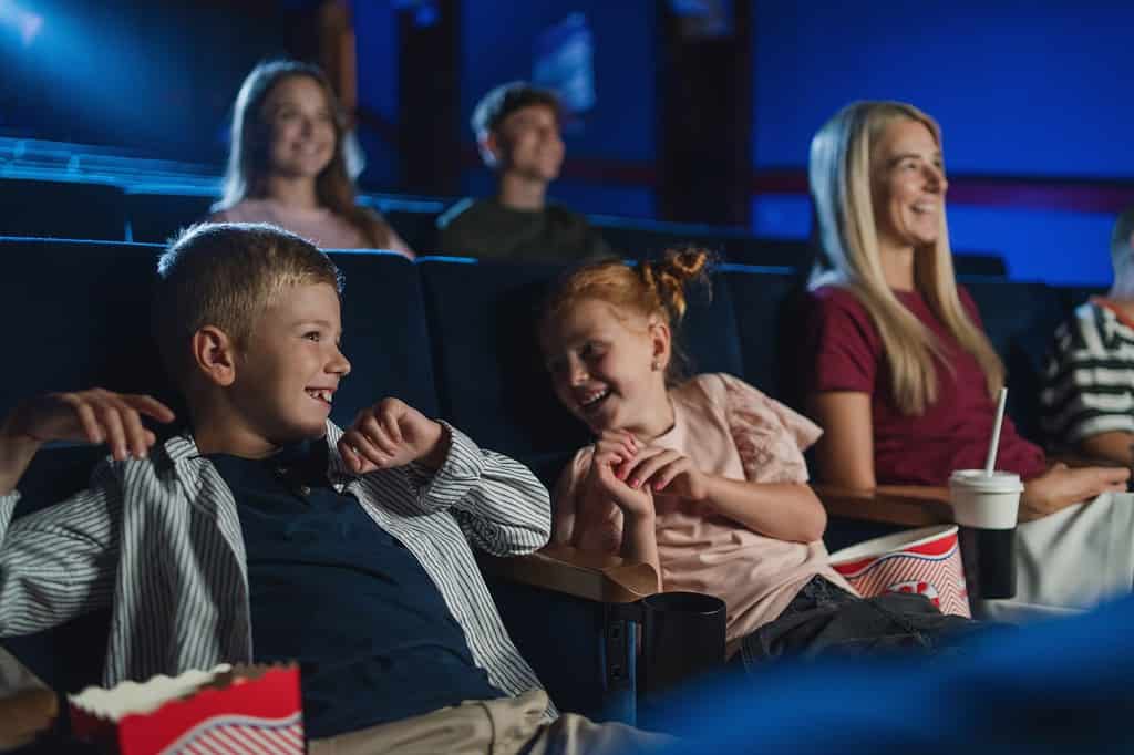 Mother with happy small children in the cinema, watching film and laughing