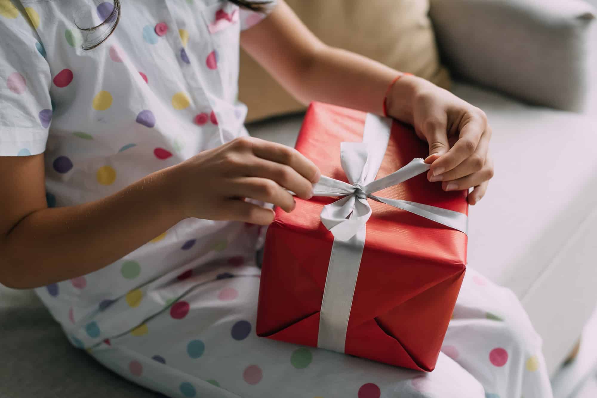 Cropped view of child in pajama holding Christmas gift with bow on couch