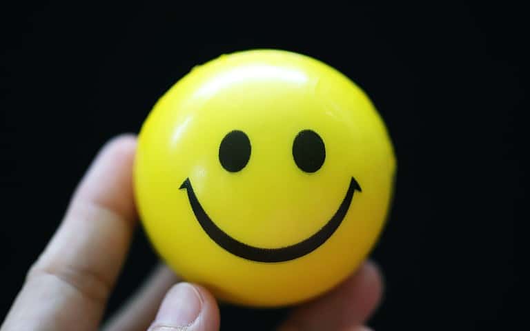 People holding yellow emoji ball with smiling face closeup on black background